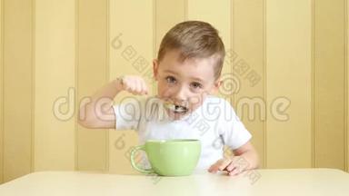 一个快乐的孩子坐在桌子旁用勺子从盘子里吃汤。